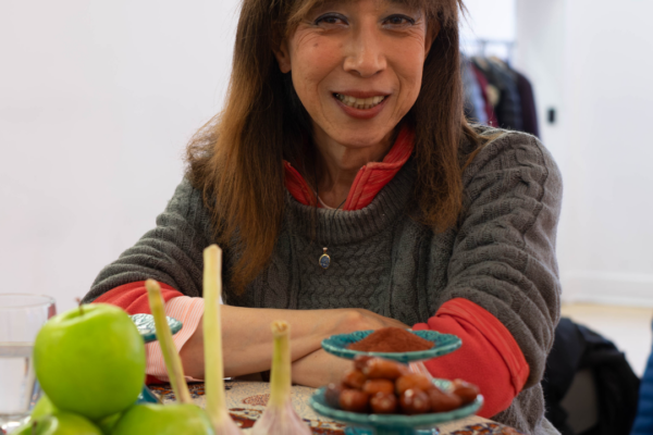 Norie standing beside the haft-seen at the older adults Nowruz celebrations.